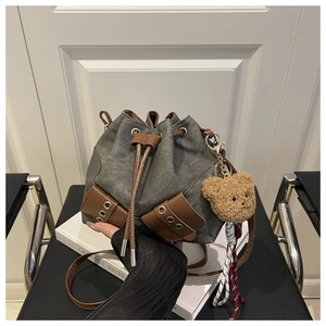 Detail of canvas drawstring bucket bag featuring leather trim and brown teddy bear charm