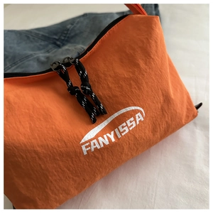 Close-up of orange nylon crossbody bag with white logo and dual black zippers