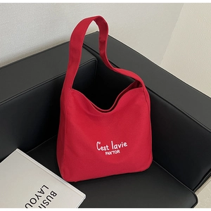 Détail du sac cabas en toile rouge avec lettrage blanc sur un canapé en cuir noir