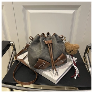Detailed close-up of charcoal canvas drawstring bucket bag with leather accents and bear charm