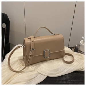 Detail of a beige leather crossbody square bag with silver metal buckle on soft fabric