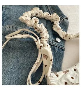Detail of cream corduroy scrunchie with brown bow and heart patterns on denim fabric