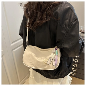 Détail du sac bandoulière crème avec broderie et breloque violette sur veste en cuir