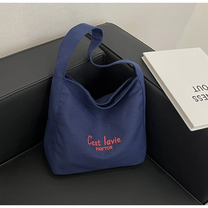 Détail d'un cabas en toile marine avec texte rouge posé sur un canapé en cuir