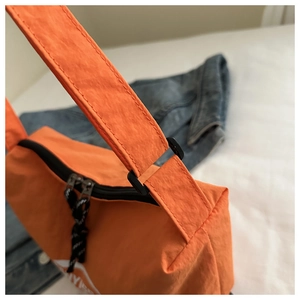 Detailed close-up of bright orange nylon crossbody bag with black buckle and logo