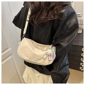 Détail du sac demi-lune crème avec pendentif violet sur l'épaule d'un modèle