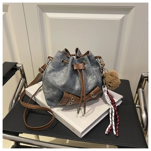 Detail of drawstring bucket bag in denim and brown leather with a cute plush bear charm