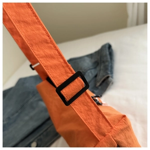 Detail of orange nylon crossbody bag showing the adjustable strap and black buckle closure