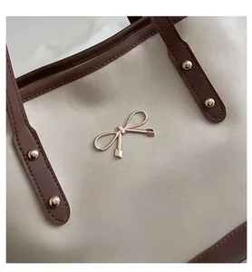 Close-up of leather tote bag with gold bow logo and elegant contrast trim detail