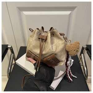 Detail view of drawstring bucket bag in beige canvas with brown leather corners and bear charm