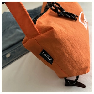Close-up of orange nylon fabric texture with black brand tag and braided zipper pull