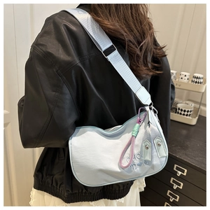 Détail du sac croissant en nylon bleu clair avec broderie de lettres et breloque colorée