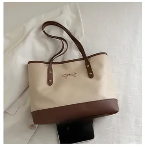 Size comparison of a minimalist contrast tote bag with mobile phone and gold bow detail