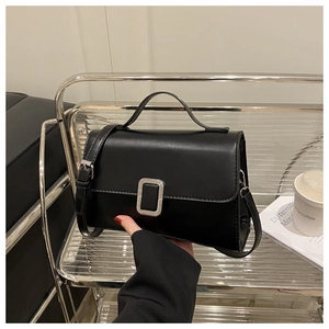 Close-up of black leather crossbody bag with silver buckle on a modern metal shelf
