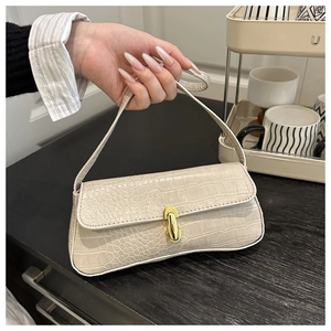 Close-up of beige crocodile pattern baguette bag with a gold capsule-shaped metal clasp