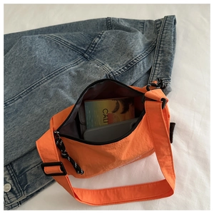 Detail view of bright orange nylon crossbody bag with black zipper and wide shoulder strap