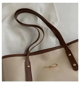 Detail of beige tote bag with brown leather trim and golden metal bow decoration