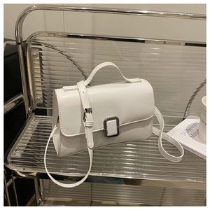 Detail shot of white matte leather crossbody bag with silver buckle on acrylic shelf