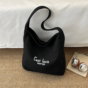 Sac hobo minimaliste en toile noire avec lettrage blanc sur un tapis tissé