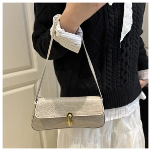 Detail view of beige crocodile embossed baguette bag with golden metal clasp on shoulder