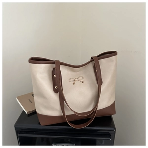 Detail of cream and brown tote bag featuring a decorative gold bow metal buckle