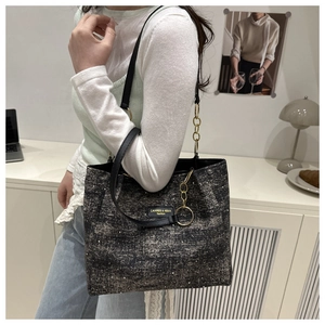 Detail of grey tweed tote bag with metal chain and leather strap on shoulder