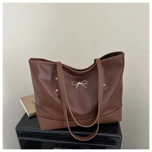 Detail of brown tote bag with golden bow buckle and decorative studs on synthetic leather