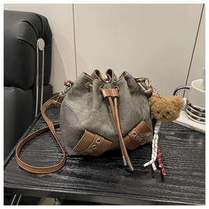 Detail of grey-green canvas bucket bag with brown leather trim and cute bear charm