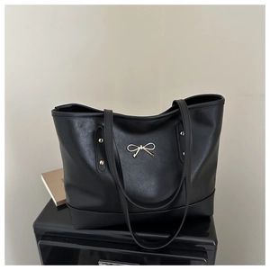 Detailed view of black matte leather tote bag featuring a golden metal bow fastener