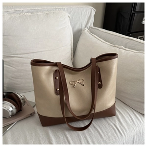Detail of two-tone beige and brown tote bag with golden bow ornament on a soft sofa