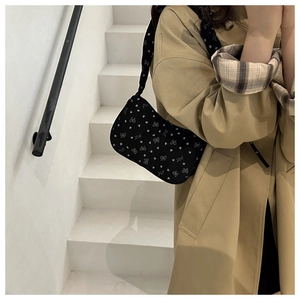 Close-up of black shoulder bag with white heart patterns and bow on khaki trench coat
