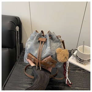 Close-up of denim drawstring bucket bag with leather pockets and plush bear charm