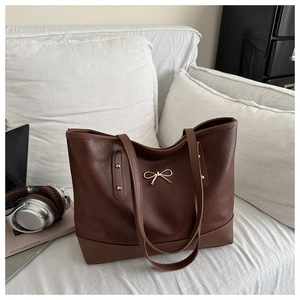 Detail view of large dark brown tote bag with gold bow buckle and laptop on a sofa