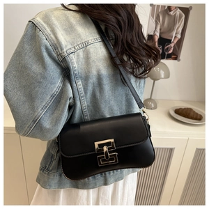 Minimalist black leather shoulder bag with gold geometric buckle worn by a model