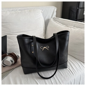 Close-up of black leather tote bag featuring a gold bow buckle in a modern office setup