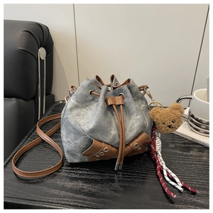 Detail of blue denim bucket bag featuring brown leather straps and plush bear charm