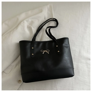 Close-up of golden bow buckle and rivet details on a black leather tote bag