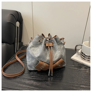 Detail of drawstring bucket bag in distressed denim with brown leather accents and strap