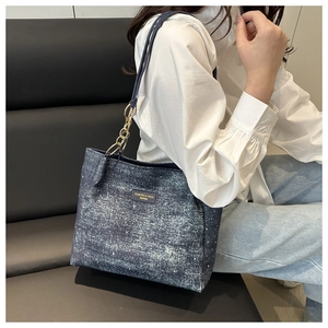 Detail of blue denim tote bag with gold chain strap and stylish logo patch