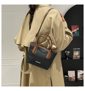 Détail du sac seau noir en cuir grainé avec poignée marron et logo métallique chic