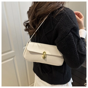 Detail of white crocodile pattern baguette bag worn on shoulder with gold twist lock