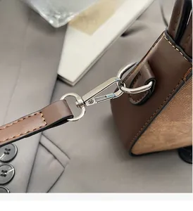 Detail of silver metallic spring hook and leather strap stitching on a brown tote bag
