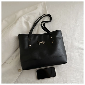 Detail of black faux leather tote bag with gold bow ornament and spacious bottom base