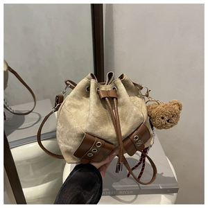 Detail of beige canvas bucket bag with brown leather drawstring and plush bear charm
