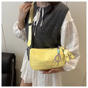 Détail d'un sac bandoulière en nylon jaune avec breloque corde violette et broderie