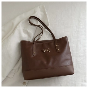 Detail of dark brown tote bag featuring golden bow hardware and faux leather texture