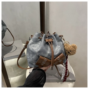 Detail of washed denim bucket bag with brown leather trim and cute bear plush charm