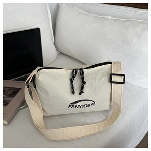 Close-up of cream nylon crossbody bag with black zipper detail on a white bed