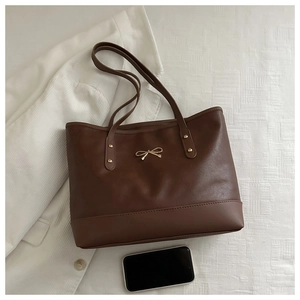 Detail view of large brown tote bag with gold bow accent and minimalist city office style