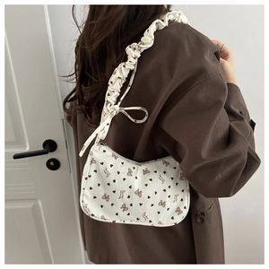 Detail showing cream corduroy shoulder bag with brown bow prints and ruffled strap